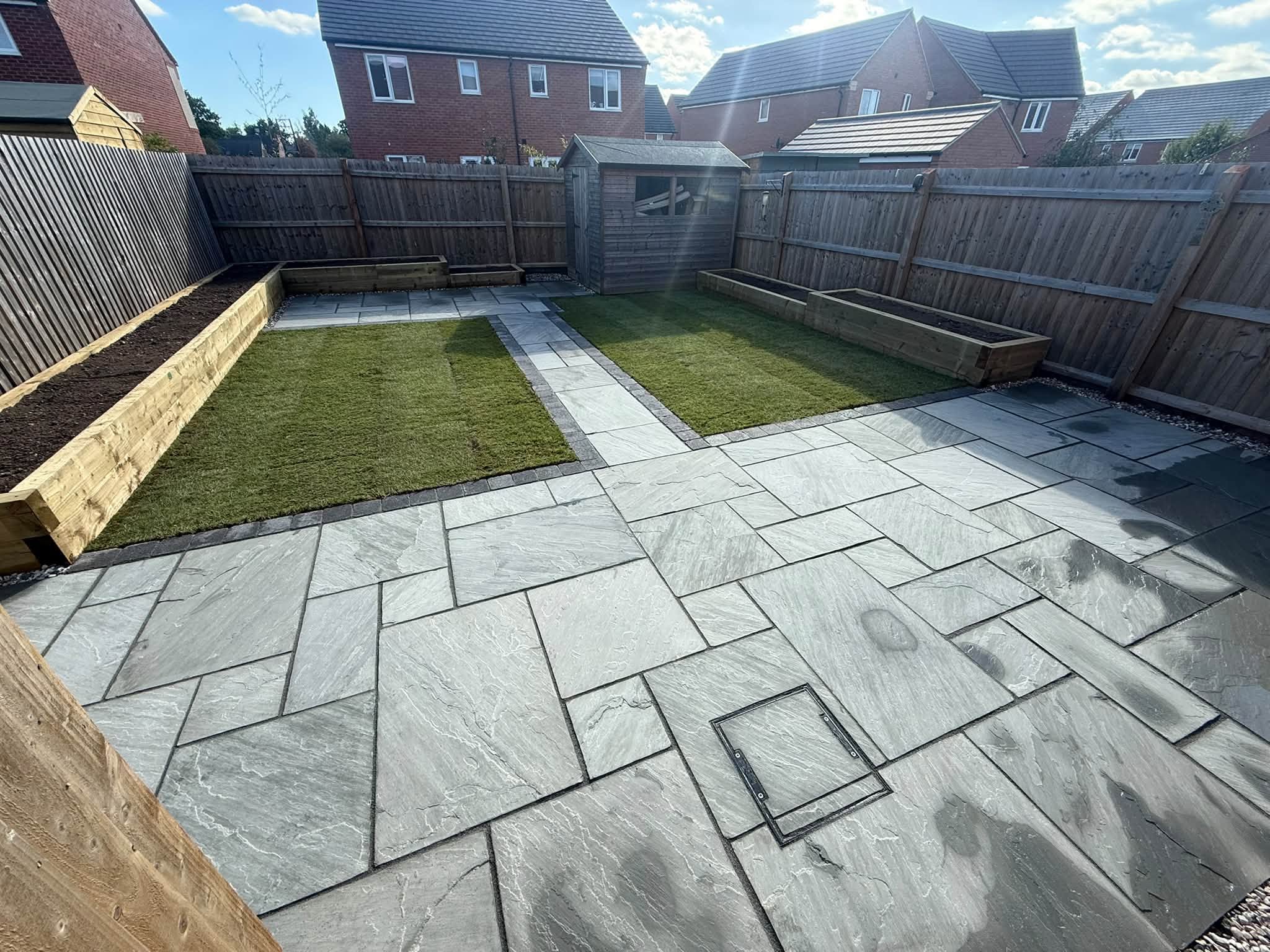 The same garden finished: grey sandstone patio framing two lawns, with sleeper raised beds along the fence