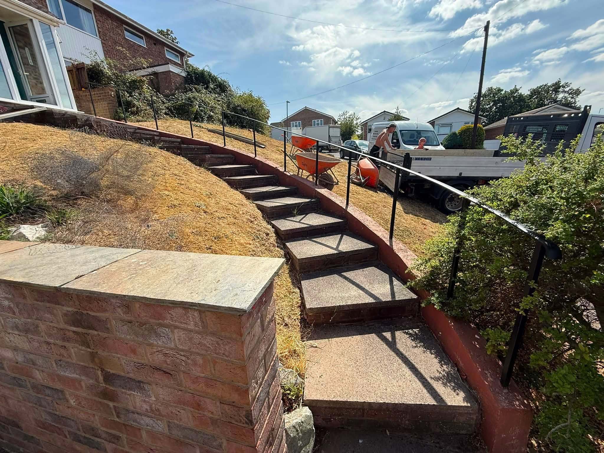 Curved brick retaining wall with steps and a handrail up a sloping garden