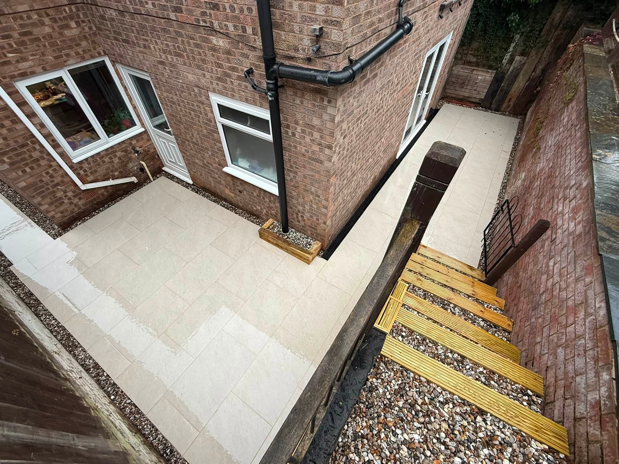 Pale paving round the back of a house with sleeper steps and gravel