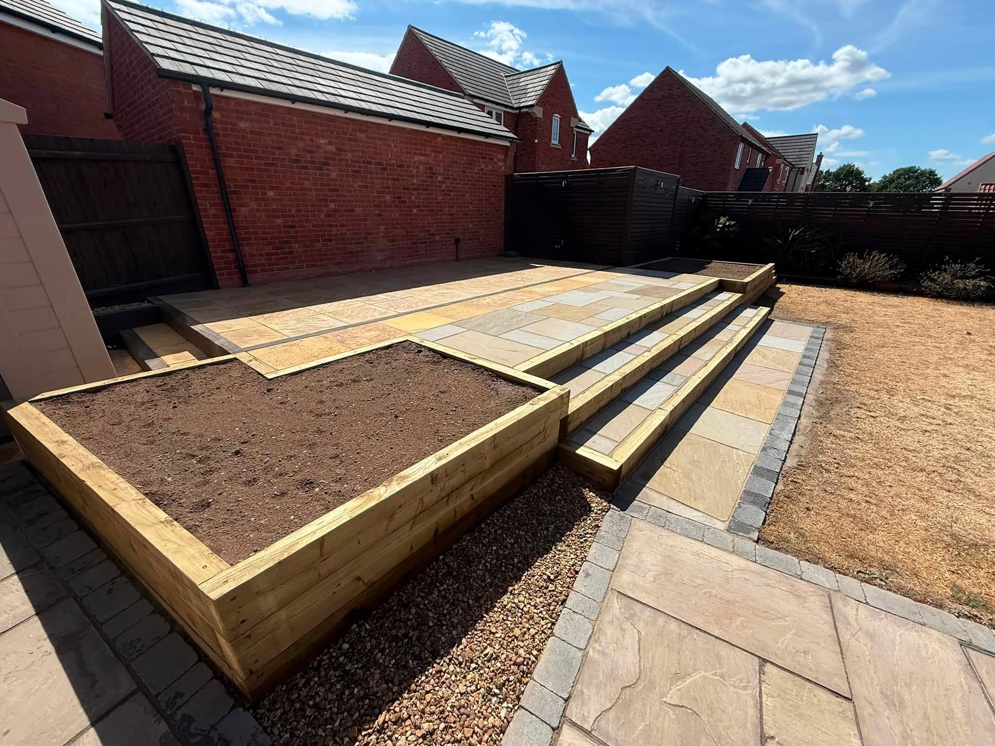 Sandstone patio with timber sleeper steps and a sleeper raised bed