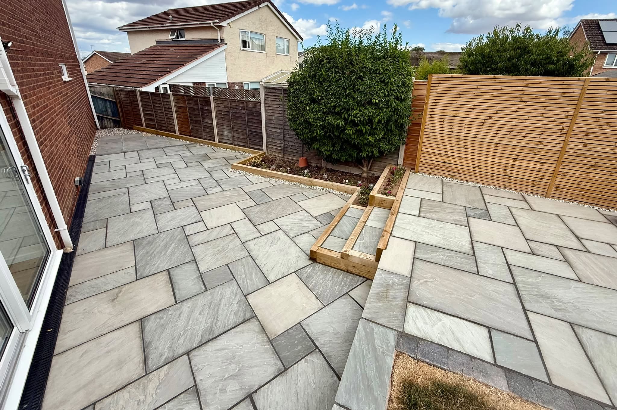 Grey sandstone patio with a sleeper planter and new fence panels