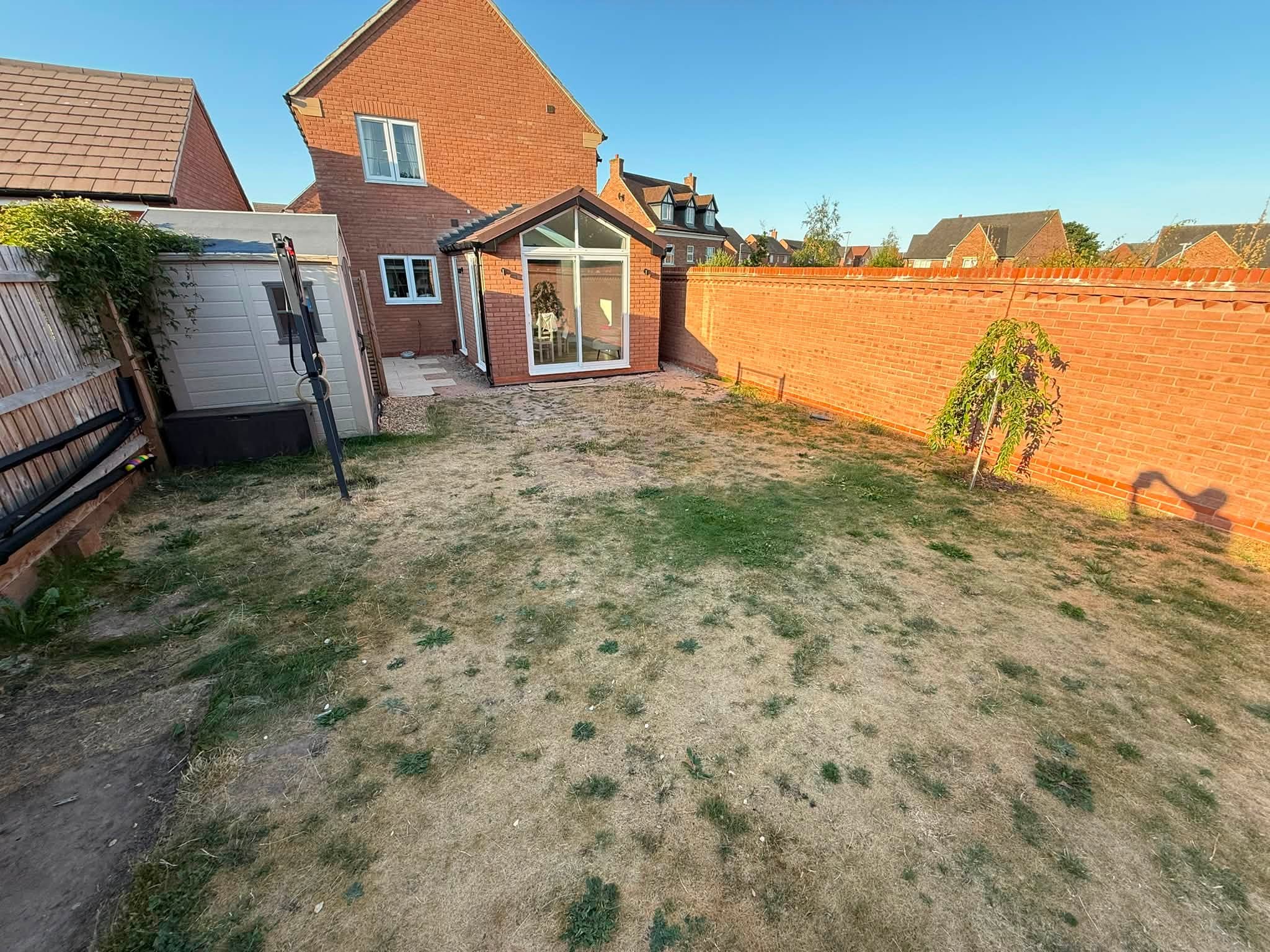 Garden before the work: dry, bare lawn behind a new-build house with a gable garden room