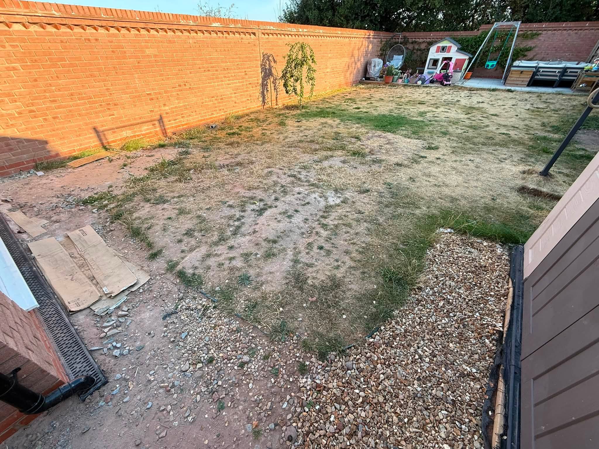 Garden before the work: patchy, worn lawn, loose gravel and old slabs against a red brick wall
