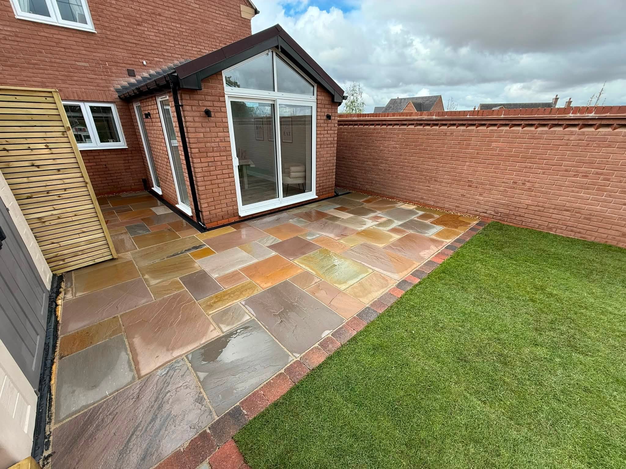 Multicolour sandstone patio and fresh turf outside a gable garden room