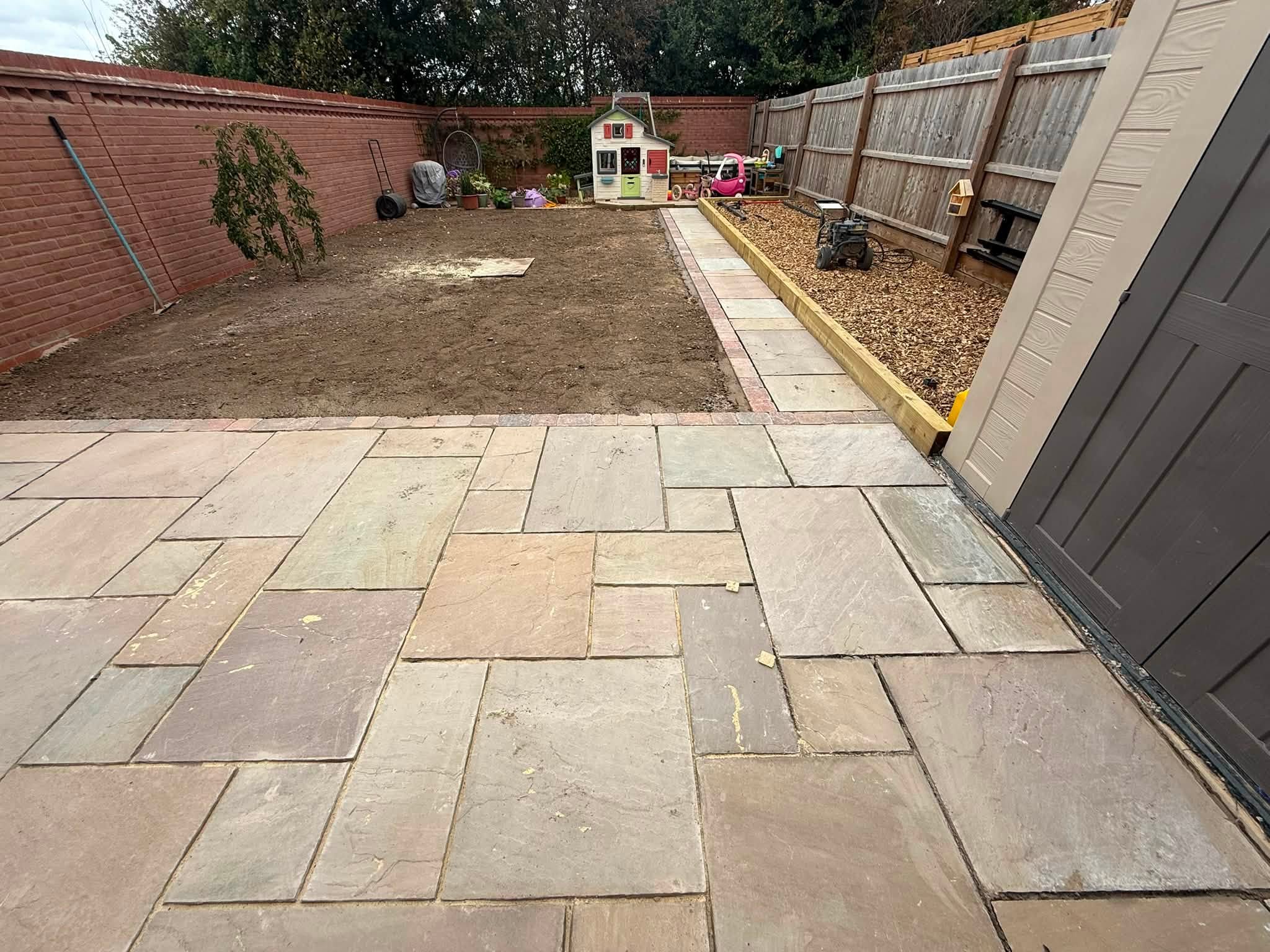 The same garden mid-build: sandstone patio laid and the ground levelled ready for turf