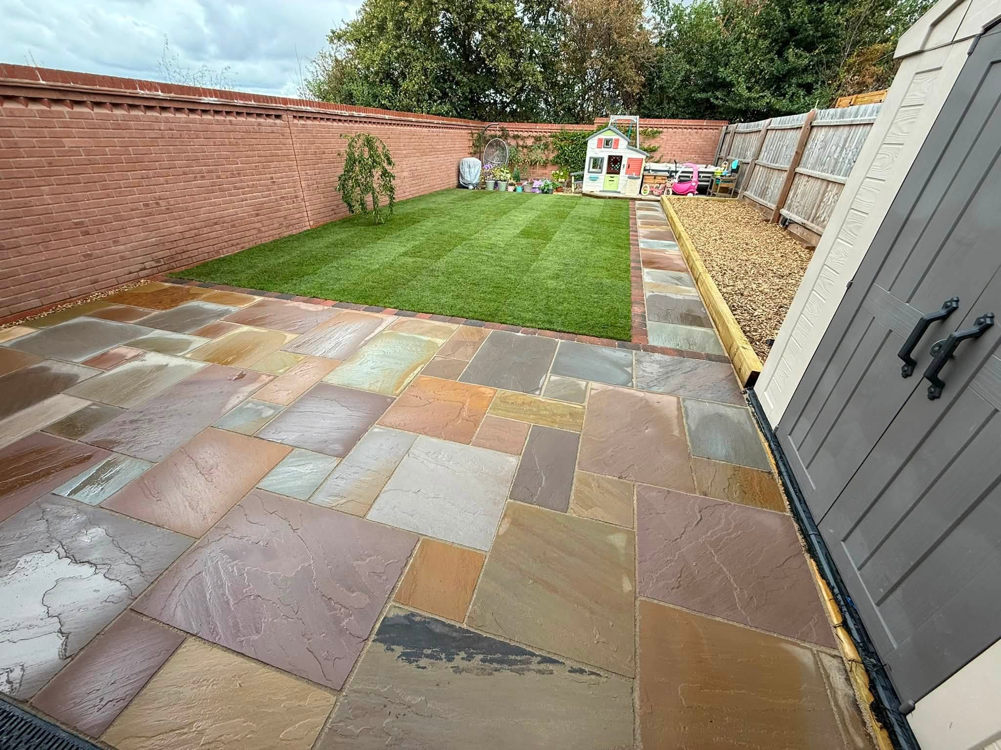 The same garden finished: multicolour sandstone patio, sleeper-edged gravel border and a new striped lawn