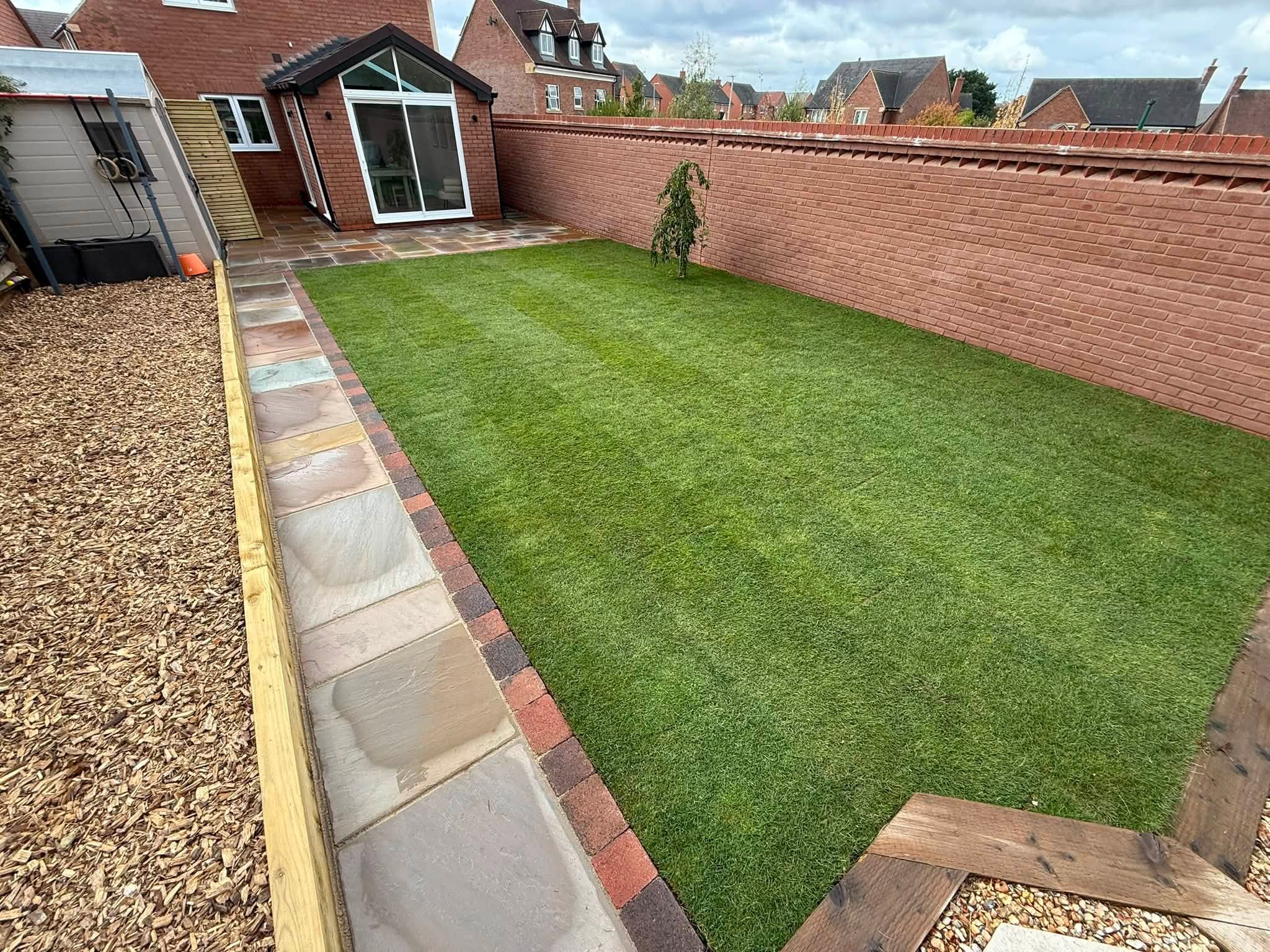 The same garden finished: fresh lawn with a sandstone path, brick edging and timber sleepers