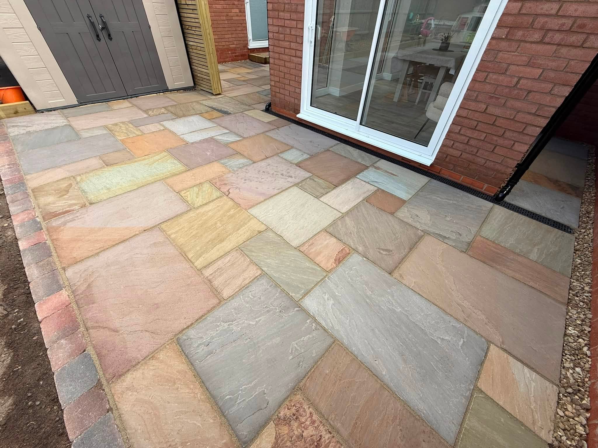 Sandstone patio outside sliding doors with a brick-edged border