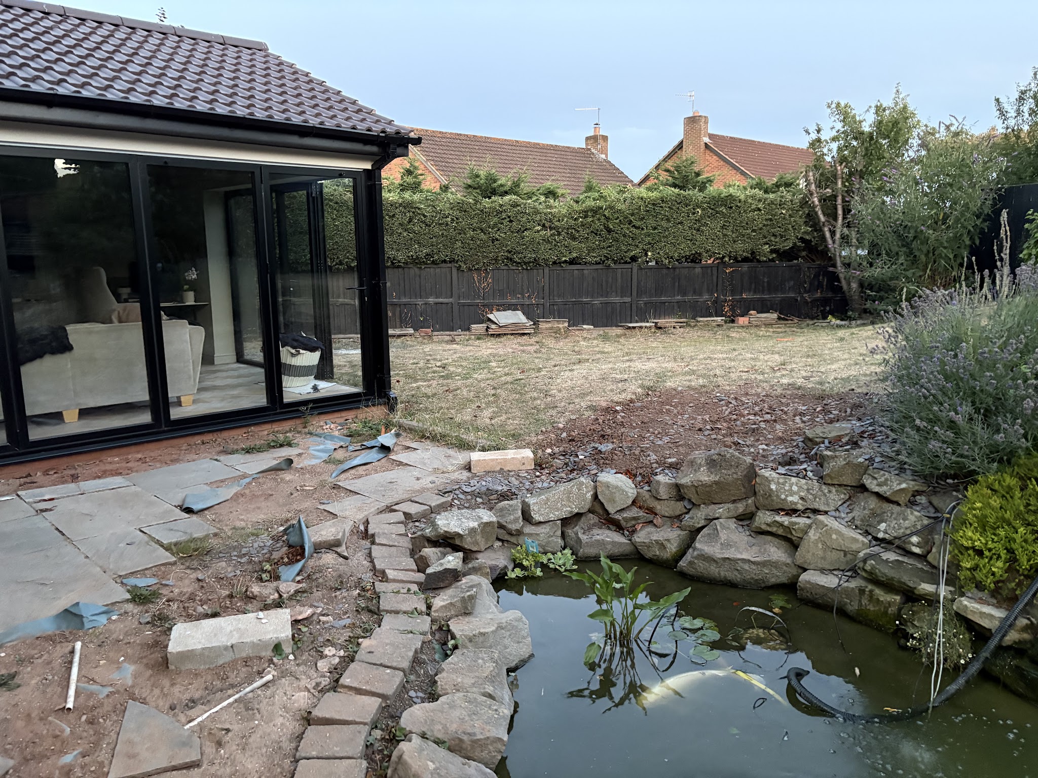 Garden before the work: old patio lifted, pond and rockery beside a garden room with black bifold doors