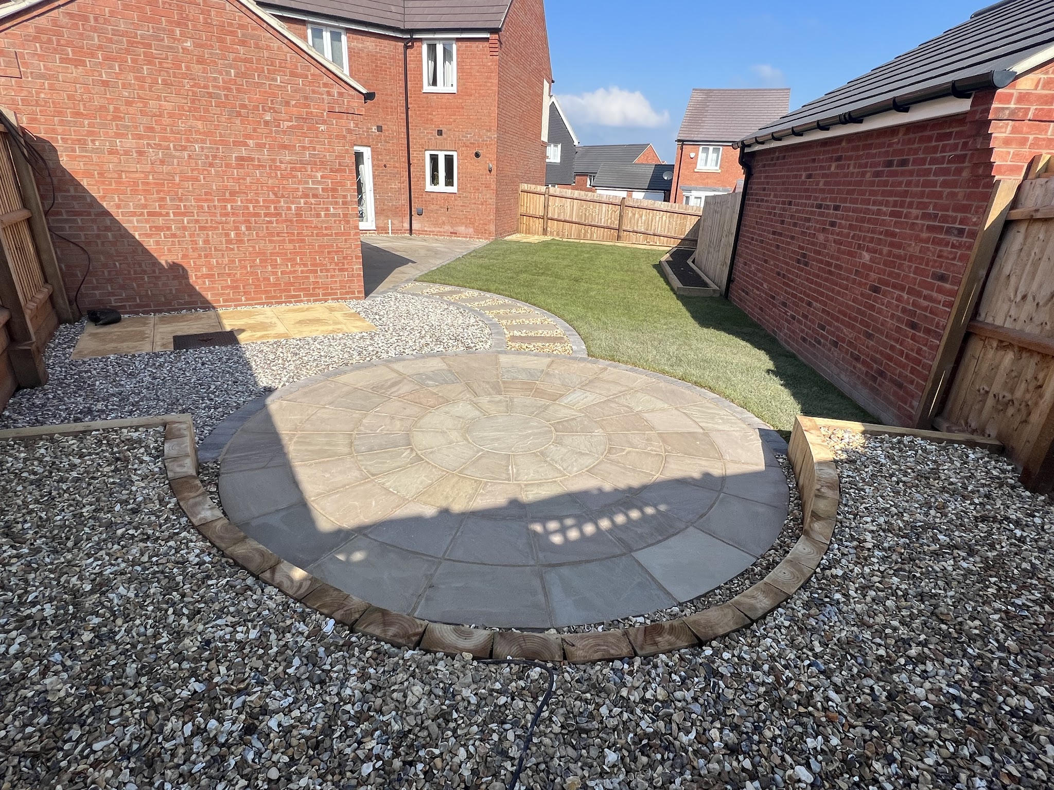 Circular sandstone patio set in grey gravel with block edging and a new lawn behind