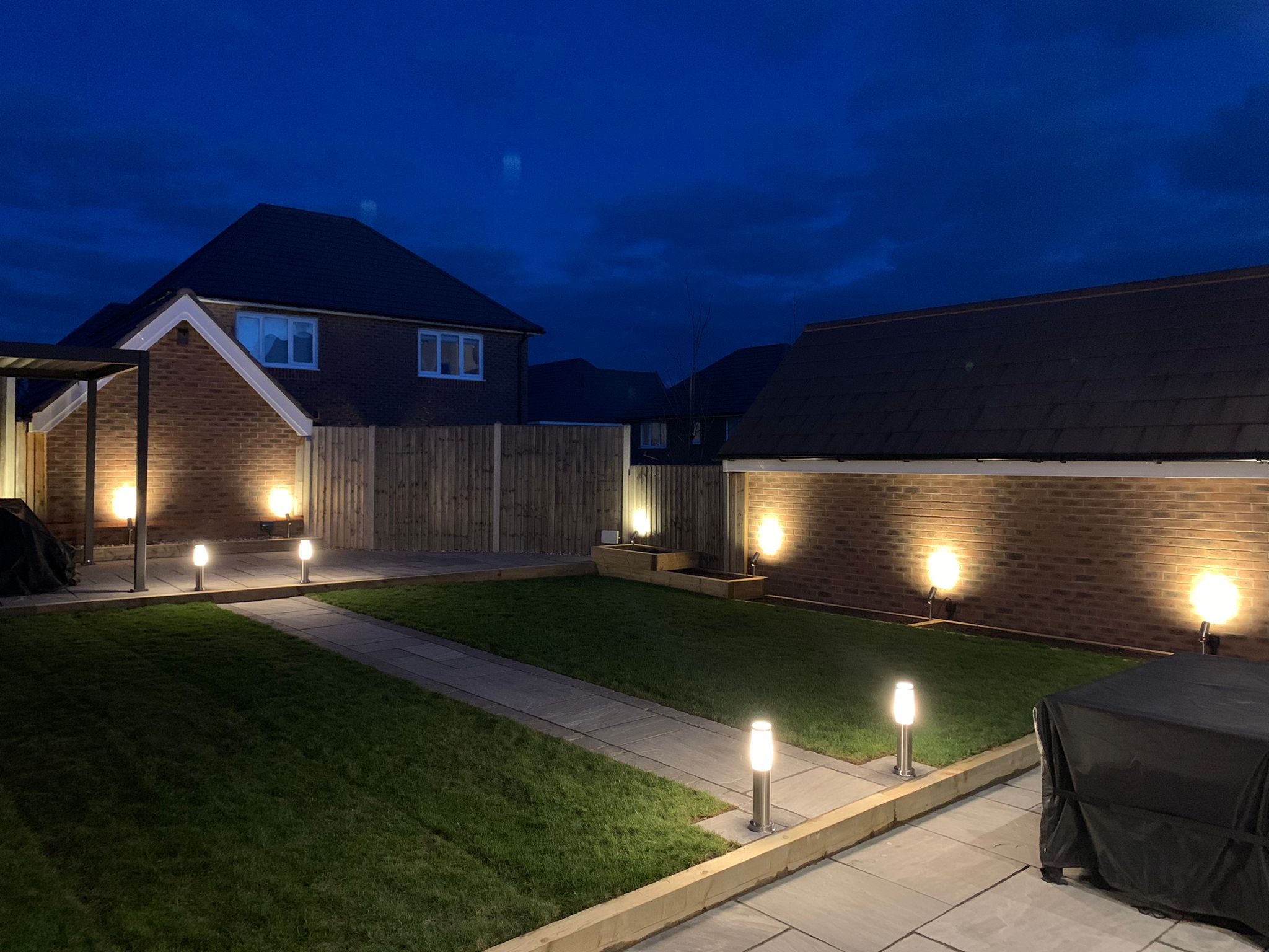 A finished garden at dusk: lawn, paved path and sleeper edging lit by garden lights