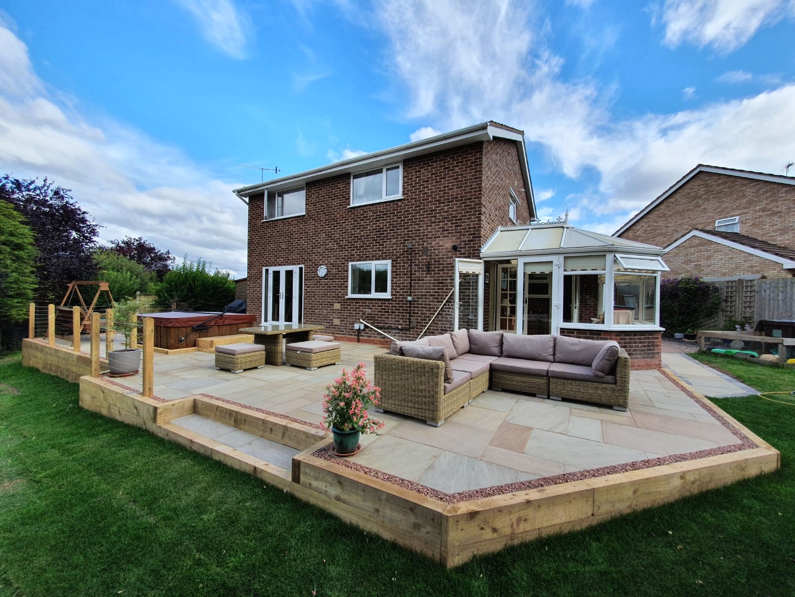 Raised sandstone patio on timber sleeper walls with steps down to a new lawn, outside a house with a conservatory