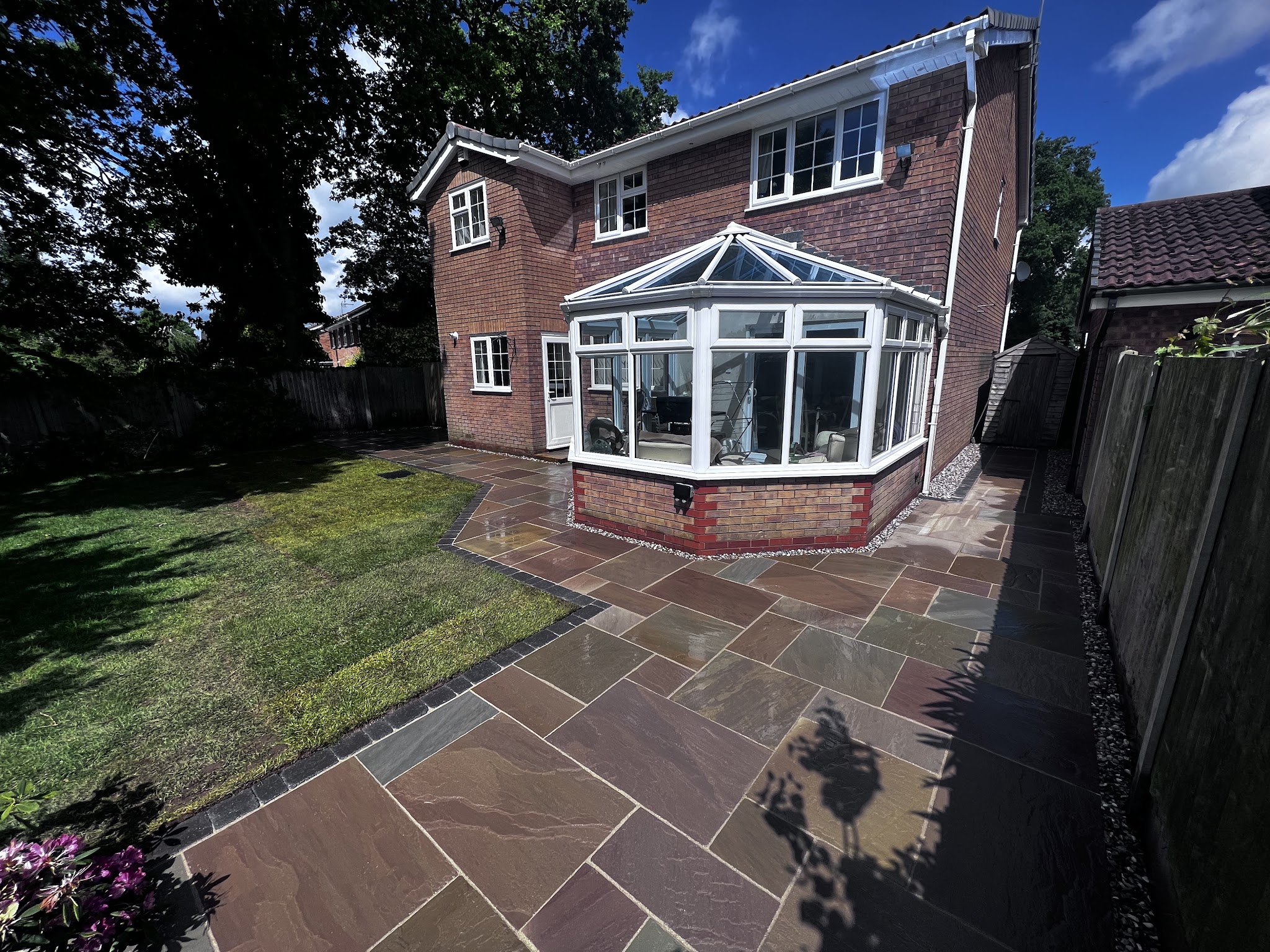 Autumn-toned sandstone patio wrapping round a conservatory, with a new lawn