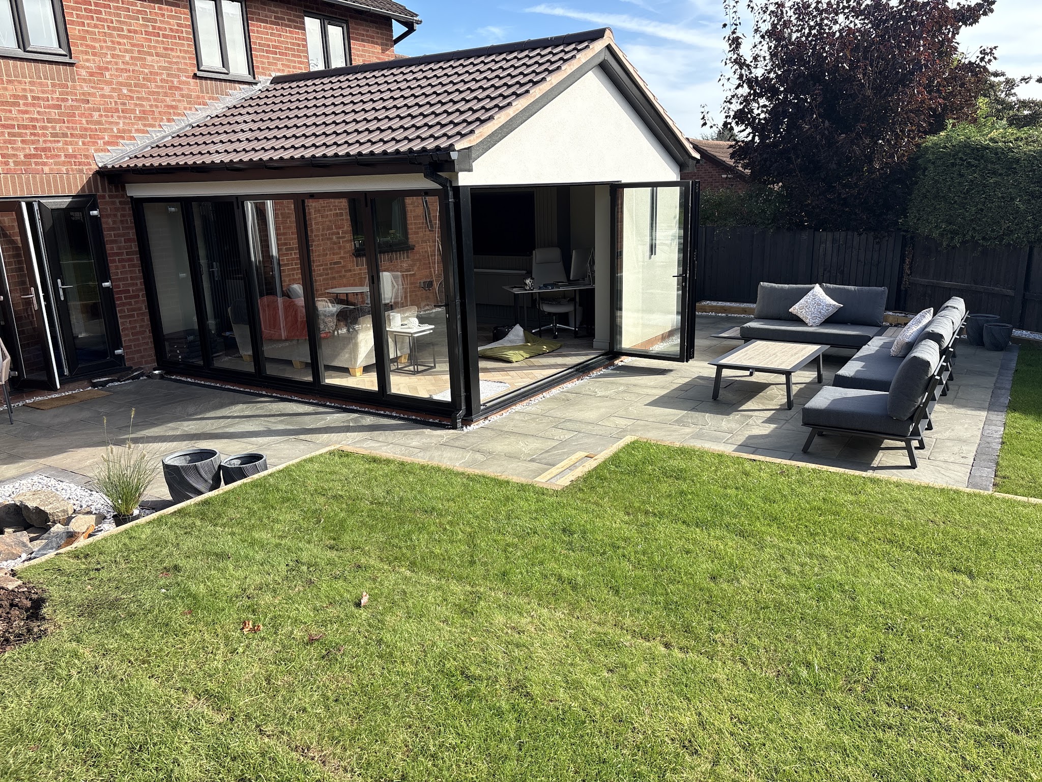 The same garden finished: grey patio outside the garden room with outdoor sofas and a new lawn